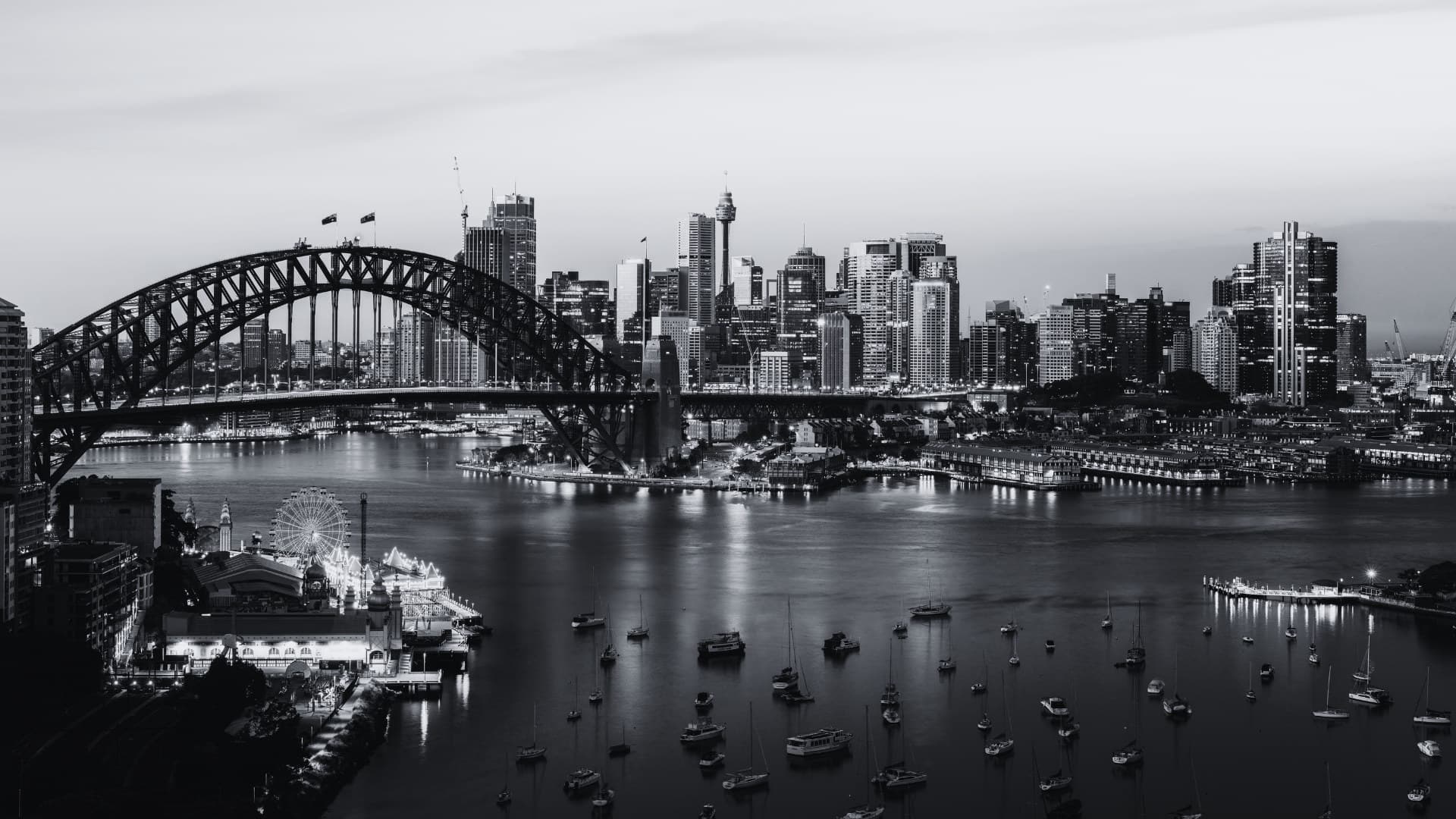 Sydney Harbour at dusk, with the Harbour Bridge, the city skyline and yachts moored in the bay.